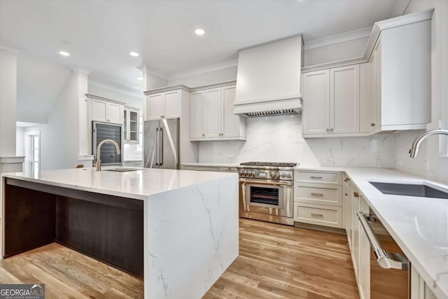 kitchen with sink, high end appliances, a center island with sink, custom range hood, and decorative backsplash