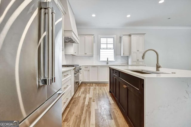 kitchen with sink, white cabinetry, backsplash, premium appliances, and light wood-type flooring