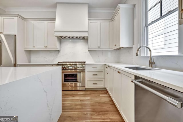 kitchen featuring appliances with stainless steel finishes, tasteful backsplash, sink, white cabinets, and custom range hood