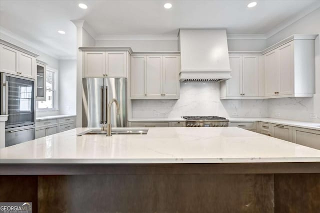 kitchen featuring high end fridge, sink, custom exhaust hood, light stone counters, and a large island with sink