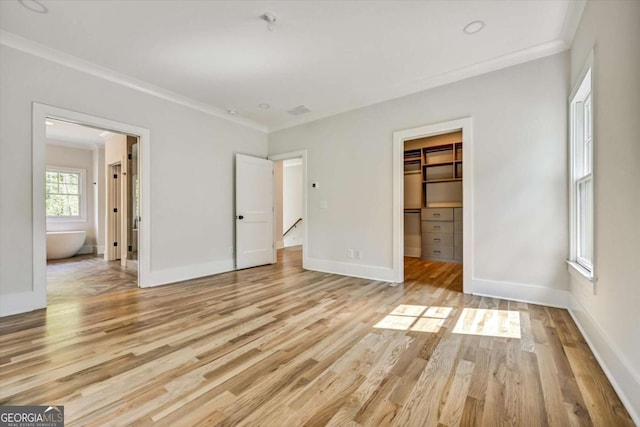 unfurnished bedroom featuring a spacious closet, light hardwood / wood-style floors, crown molding, ensuite bath, and a closet