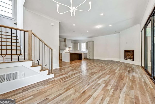 unfurnished living room with ornamental molding, an inviting chandelier, and light wood-type flooring