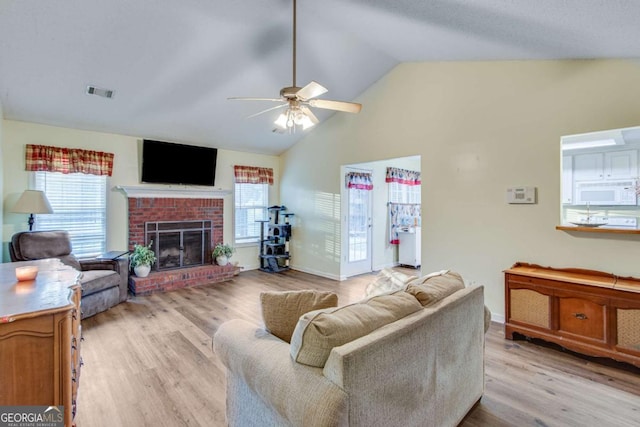 living room featuring vaulted ceiling, ceiling fan, a fireplace, and light hardwood / wood-style floors