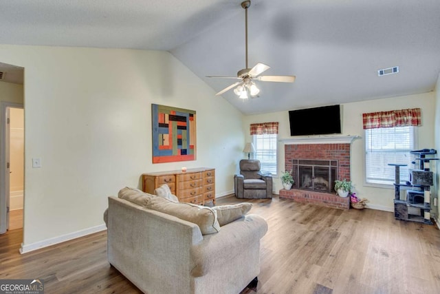 living room featuring vaulted ceiling, plenty of natural light, wood-type flooring, and a brick fireplace