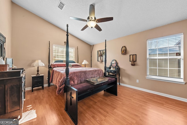 bedroom with vaulted ceiling, light wood-type flooring, a textured ceiling, and ceiling fan