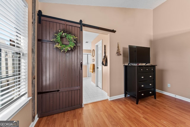 bedroom with a barn door, vaulted ceiling, and light hardwood / wood-style flooring