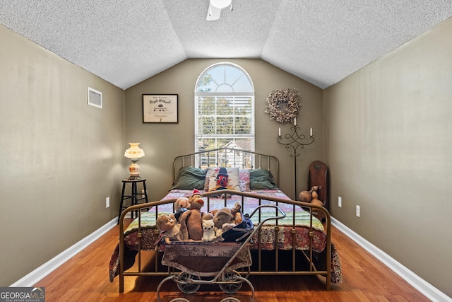 bedroom with hardwood / wood-style flooring, vaulted ceiling, and a textured ceiling