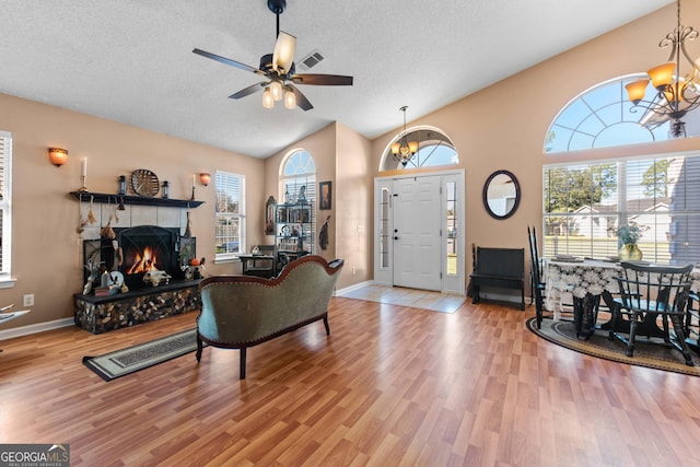 living room with a healthy amount of sunlight, a textured ceiling, a tiled fireplace, vaulted ceiling, and light wood-type flooring