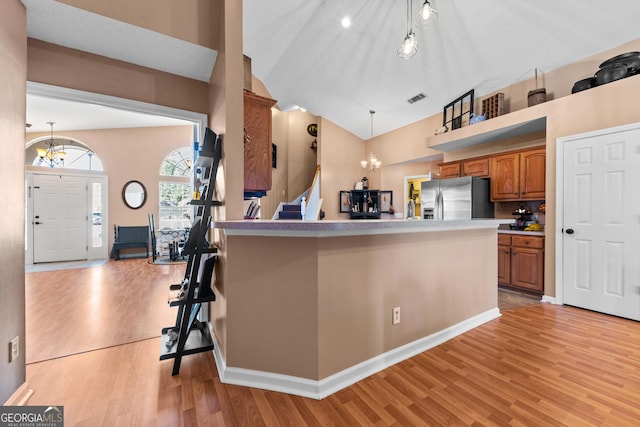 kitchen with stainless steel refrigerator with ice dispenser, a notable chandelier, light wood-type flooring, and decorative light fixtures