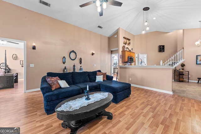 living room with ceiling fan with notable chandelier, vaulted ceiling, and light wood-type flooring