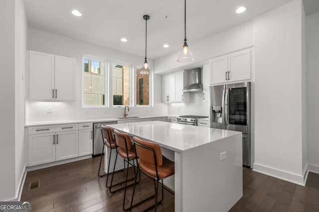 kitchen featuring sink, appliances with stainless steel finishes, white cabinets, a kitchen island, and wall chimney exhaust hood