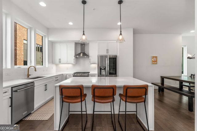 kitchen with stainless steel appliances, a center island, sink, and wall chimney range hood