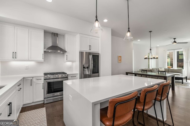 kitchen with wall chimney range hood, appliances with stainless steel finishes, white cabinetry, tasteful backsplash, and a kitchen island