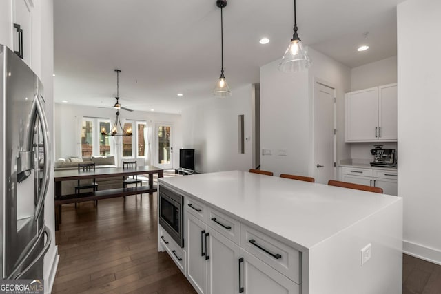 kitchen featuring white cabinetry, decorative light fixtures, appliances with stainless steel finishes, dark hardwood / wood-style floors, and a kitchen island