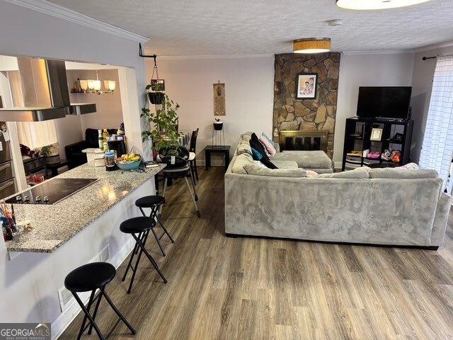 living room featuring crown molding, a fireplace, a textured ceiling, and hardwood / wood-style flooring