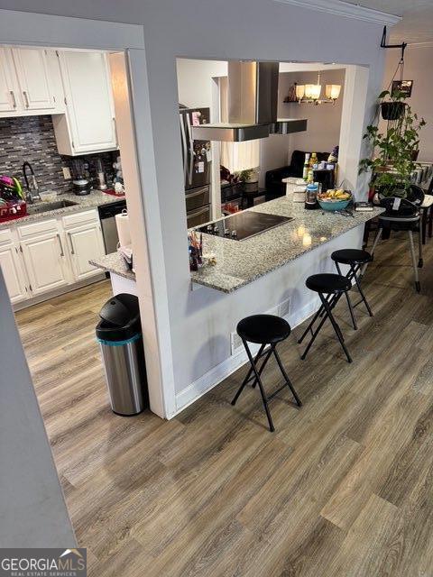 kitchen with white cabinetry, a kitchen breakfast bar, light stone countertops, wall chimney range hood, and black electric cooktop