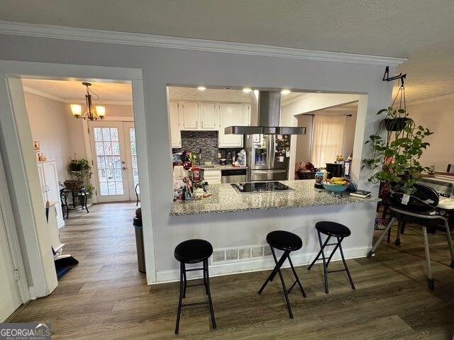 kitchen with stainless steel fridge, white cabinets, a kitchen bar, and wall chimney exhaust hood