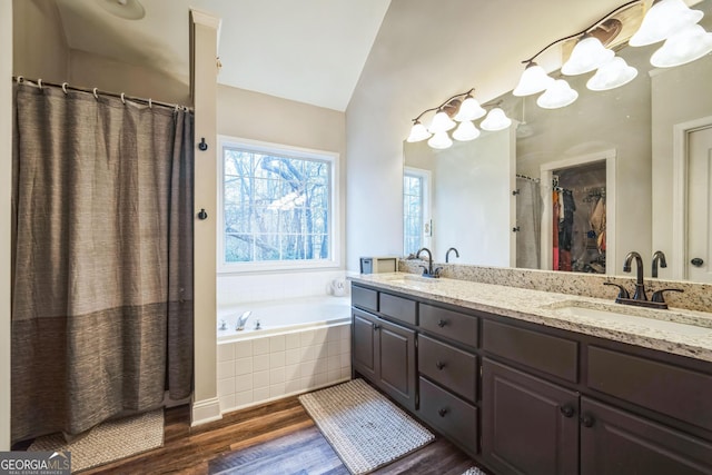 bathroom with vaulted ceiling, hardwood / wood-style floors, vanity, and tiled bath