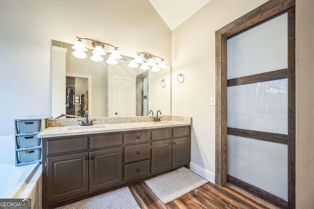 bathroom with hardwood / wood-style flooring, lofted ceiling, tiled bath, and vanity