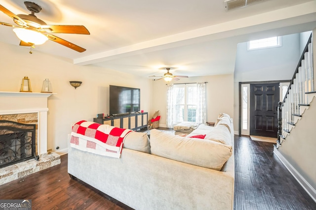 living room featuring ceiling fan, a stone fireplace, dark wood-type flooring, and beam ceiling