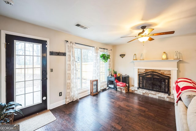 living room featuring ceiling fan, a stone fireplace, and dark hardwood / wood-style flooring