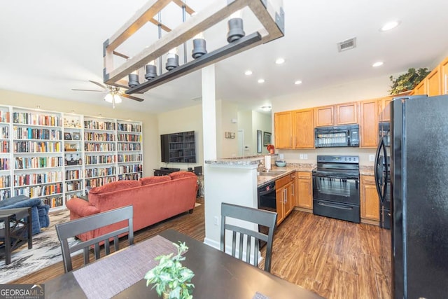 kitchen featuring dark hardwood / wood-style floors, black appliances, light stone counters, kitchen peninsula, and ceiling fan