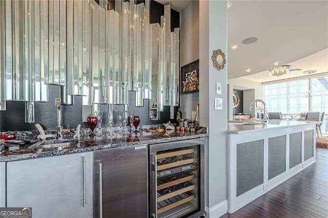 bar with sink, dark wood-type flooring, wine cooler, and dark stone counters