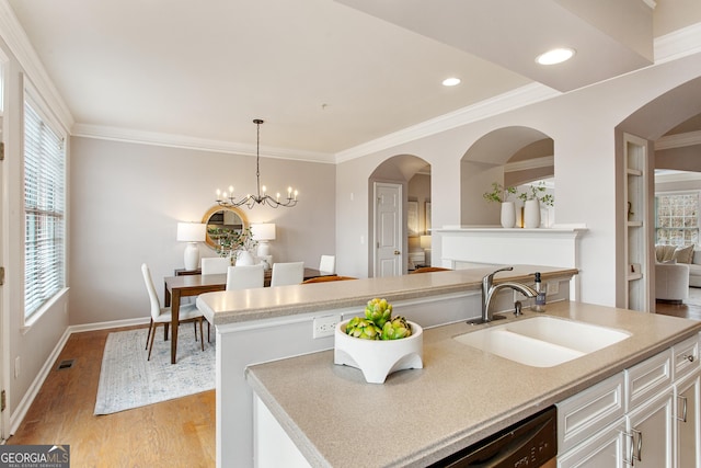 kitchen with sink, a center island with sink, light hardwood / wood-style flooring, a notable chandelier, and pendant lighting