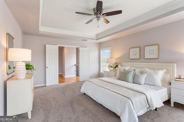 carpeted bedroom featuring crown molding, ceiling fan, and a raised ceiling