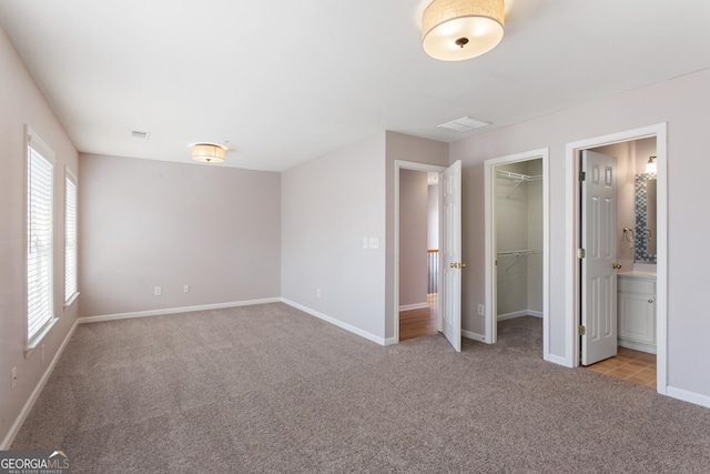 unfurnished bedroom with connected bathroom, a spacious closet, light colored carpet, and a closet