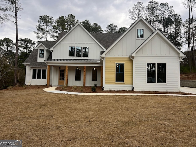 modern farmhouse style home featuring board and batten siding, a shingled roof, a front yard, covered porch, and a standing seam roof