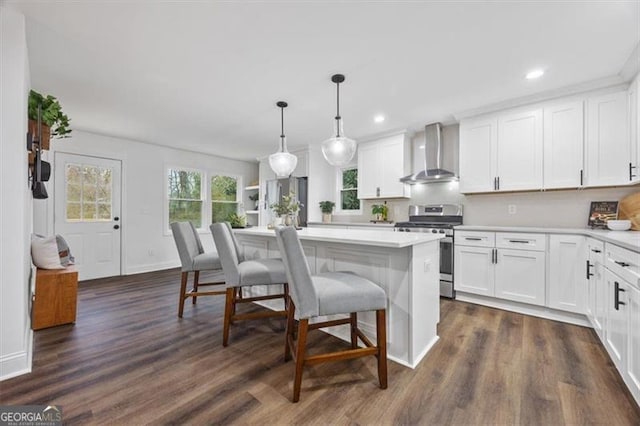 kitchen with wall chimney range hood, hanging light fixtures, a kitchen island, white cabinets, and stainless steel range oven