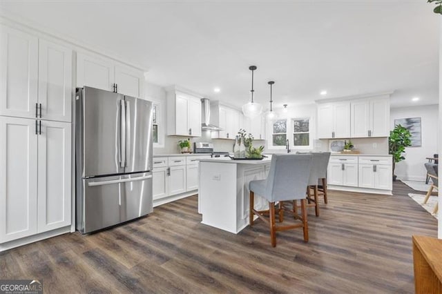 kitchen featuring white cabinets, decorative light fixtures, stainless steel appliances, and wall chimney exhaust hood