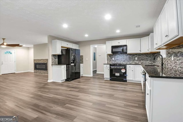 kitchen featuring white cabinets, a stone fireplace, sink, and black appliances