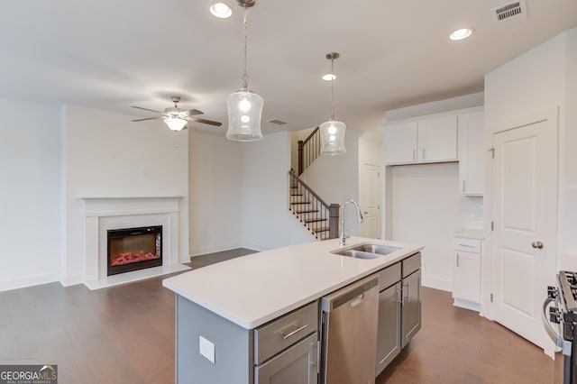 kitchen with pendant lighting, sink, white cabinets, stainless steel appliances, and a center island with sink