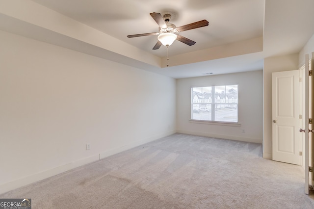 spare room with ceiling fan, light colored carpet, and a raised ceiling