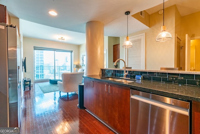 kitchen with sink, dark hardwood / wood-style flooring, dark stone counters, hanging light fixtures, and stainless steel appliances