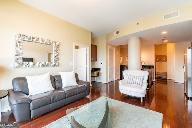 living room featuring ornate columns and dark wood-type flooring