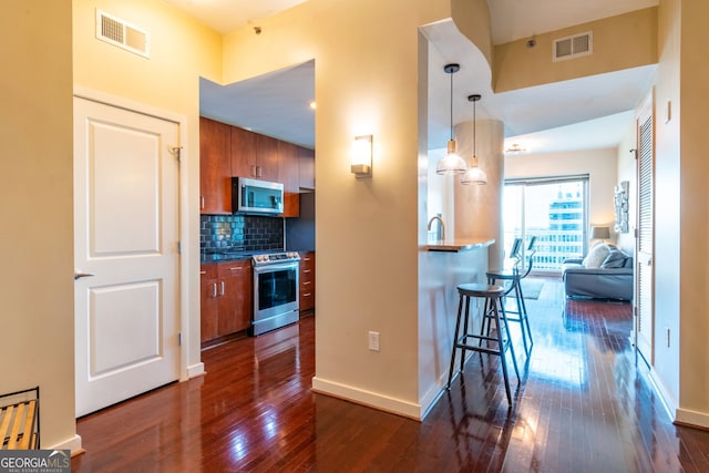 kitchen with decorative light fixtures, backsplash, a kitchen breakfast bar, stainless steel appliances, and dark wood-type flooring