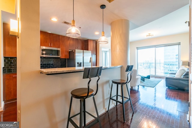 kitchen featuring a breakfast bar, dark hardwood / wood-style floors, decorative backsplash, kitchen peninsula, and stainless steel appliances