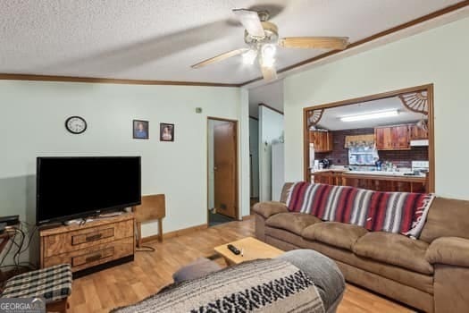 living room featuring lofted ceiling, light hardwood / wood-style flooring, a textured ceiling, ornamental molding, and ceiling fan