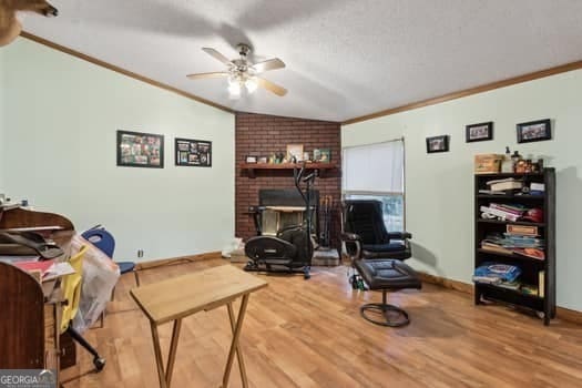 sitting room featuring crown molding, wood-type flooring, vaulted ceiling, a textured ceiling, and ceiling fan