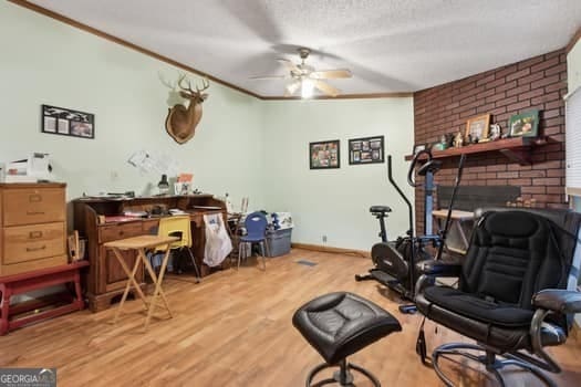 exercise room with crown molding, ceiling fan, a fireplace, a textured ceiling, and light wood-type flooring