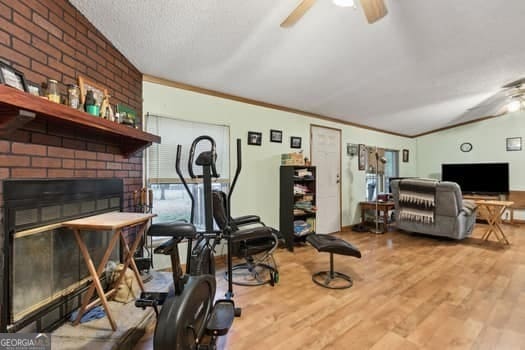 workout room with crown molding, ceiling fan, hardwood / wood-style floors, a fireplace, and a textured ceiling