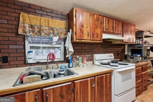 kitchen featuring brick wall, sink, white electric range, and a textured ceiling