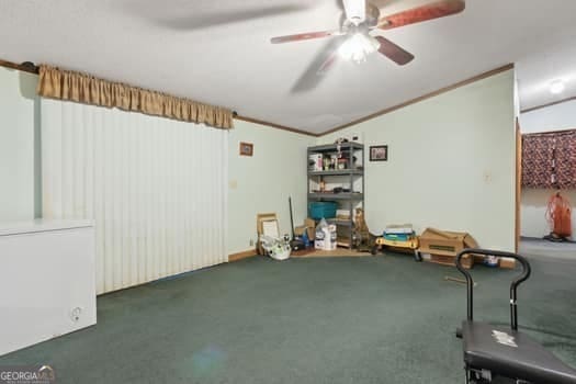 interior space featuring crown molding, ceiling fan, and dark colored carpet