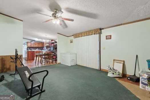 workout room featuring crown molding, ceiling fan, wooden walls, carpet floors, and a textured ceiling