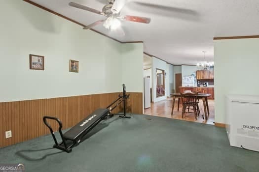 exercise room featuring ceiling fan with notable chandelier, wooden walls, and ornamental molding