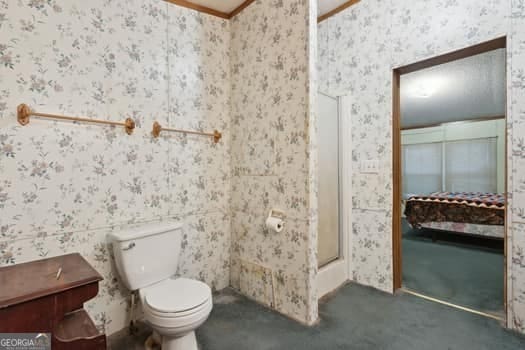 bathroom featuring crown molding, a shower with shower door, and toilet