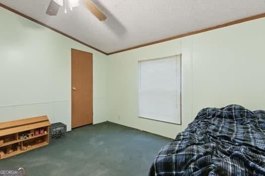 bedroom featuring crown molding, vaulted ceiling, a textured ceiling, dark carpet, and ceiling fan